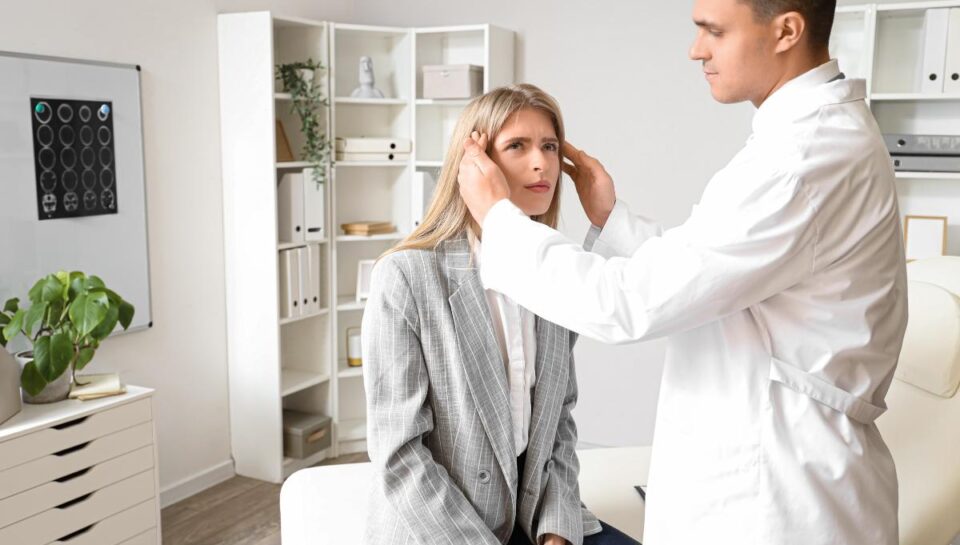 ### Key Elements

- **Main Subjects**: A young woman and a male doctor.
- **Objects**: Medical examination tools, a chair, and a whiteboard.
- **Notable Features**: The doctor is wearing a white coat; the woman is in a casual outfit with a blazer.
- **Text/Symbols**: A whiteboard with medical imagery or charts in the background.
  
### Overall Mood/Theme

The scene conveys a professional medical environment focused on patient care. The expressions of both the doctor and the woman suggest a serious yet calm atmosphere, indicating a routine medical examination. The setting is clean and organized, reinforcing a sense of professionalism and trust.
